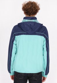 Lichte, gewatteerde jas met capuchon, uitgerust met een mintgroene bovenkant, marineblauwe mouwen en contrasterende stiksels voor extra detail. Gladde textuur, casual pasvorm.