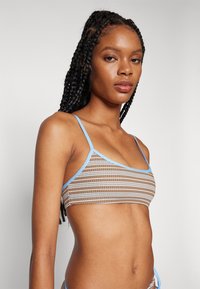 Top bikini marrone e blu a fantasia con spalline sottili, caratterizzato da un design geomtrico e bordi a contrasto, texture liscia e copertura minimale.