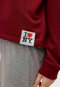 Burgundská mikina s bílou etiketou se červeným srdcem a černým textem "I ♥ NY." Stylová s šedými kalhotami, zdůrazňující bavlněnou strukturu a ležérní design.