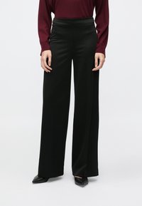 Pantaloni negri cu picioare largi, dintr-un material neted, cu talie înaltă și croială lejeră. Purtați cu un top grena cu mâneci lungi și pantofi cu toc negri.