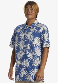 Camisa de manga corta, tipo camisa, hecha de tela azul con patrones de hojas de palma blancas y acentos rosas, con un collar clásico y un ajuste relajado.