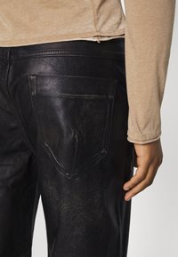 Black leather pants with a textured finish, featuring a back pocket. A beige long-sleeve shirt is partially visible.