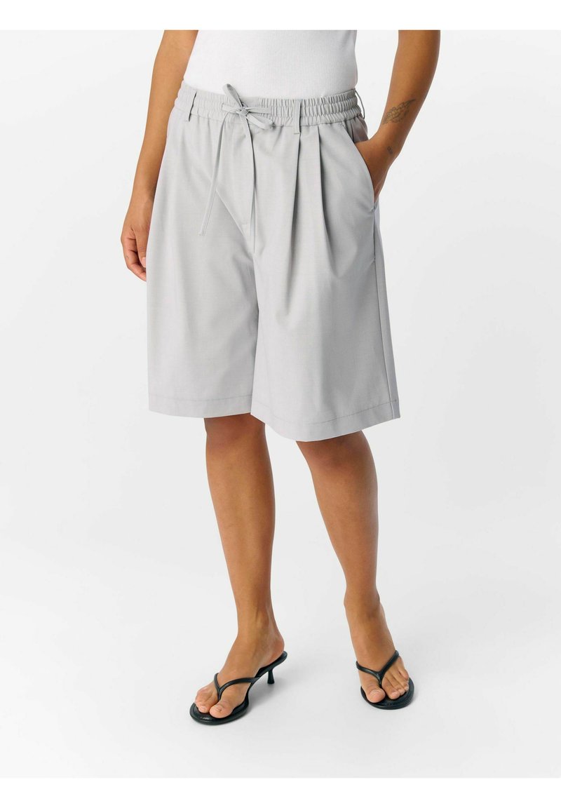 Pantaloni shorts grigi chiari realizzati in tessuto morbido, con vita regolabile tramite cordoncino e pieghe, dotati di tasche laterali e design lunghezza ginocchio.