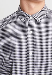 Primo piano di una persona che indossa una camicia a scacchi bianchi e neri con colletto button-down.