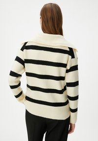 Cremfarbener Pullover mit schwarzen horizontalen Streifen, geripptem Kragen und Bündchen, weichem Material, lockerer Passform und lässigem Design.
