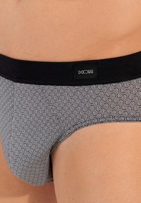 Zwart-wit gestreepte slipjes met een gladde textuur en een elastische tailleband met een logo-label, die het golfpatroon benadrukken.