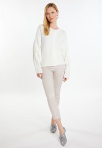 Witte, ribbelgebreide cardigan met drie knopen, gecombineerd met lichtbeige goed passende broek en grijze schoenen met decoratieve gespen.