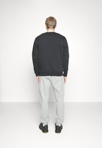 Felpa nera con polsini a coste, abbinata a pantaloni della tuta grigi chiari con polsini elastici. Scarpe nere con suola in gomma completano l'outfit.