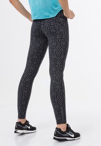 Leggings neri con un motivo floreale e dettagli bianchi, design aderente, abbinati a scarpe da corsa nere e una maglietta azzurro chiaro.