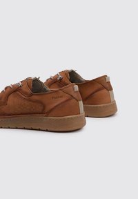 Zapatos de cuero marrón con una parte superior texturizada, que presenta perforaciones y una suela de goma. Los cordones son grises, con un acento de color beige claro en el talón.
