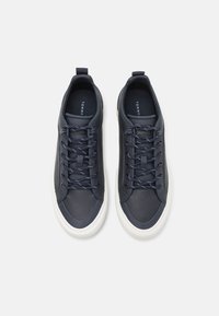 Elegante navyblaue Sneaker mit strukturierter Oberfläche, dunklen Schnürsenkeln und weißen Gummisohlen. Der Markenname "TOMMY" ist auf den Einsätzen sichtbar.