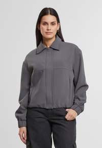 Gray, collared jacket with a front zip, elastic cuffs, and a smooth texture. Features two horizontal seam lines on the front.