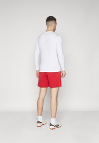 T-shirt de sport à manches longues blanche et shorts rouges, associés à des chaussures de sport légères avec des accents noirs et orange. Design simple, sans motifs.