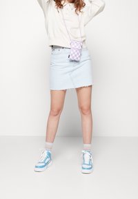 Minifalda de mezclilla azul claro con dobladillo deshilachado, combinada con zapatillas blancas y azules y un bolso bandolera a cuadros lavanda.