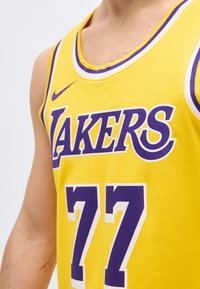Κίτρινη μπασκετική φανέλα με μοβ κείμενο "Lakers" και αριθμό 77, που φοριέται από ένα άτομο, εμφανίζοντας το πάνω μέρος του στήθους και το μπράτσο.