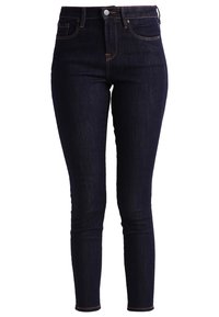 Högmidjade mörkblå denimskinnyjeans med en slät текстur, fem fickor, knäppning och dragkedjestängning, samt kontrasterande sömnadsdetaljer.