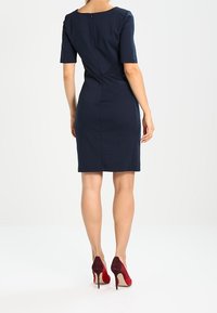 Marinblå klänning med korta ärmar och dragkedja i ryggen. Röda och vinröda tvåtonade högklackade skor fulländar looken.