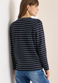 Chemise à manches longues rayée bleu marine avec un col rond et une texture douce, associée à un jean en denim bleu clair, vue de dos.