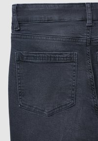 Jeans en denim foncé avec une texture lisse, deux poches arrière avec des bords cousus et un design de taille ajustée.