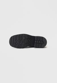 Suela de zapato de goma negra con surcos profundos, con el nombre de la marca "REPLAY" en relieve en el centro y varios patrones texturizados para mejorar la tracción.
