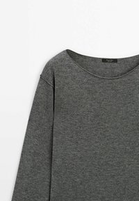 Pull-over gris en tissu doux, avec un large décolleté et des manches longues à coupe décontractée. Surface simple et texturée.