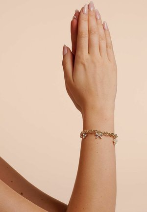 Two hands pressed together vertically with polished nails, wearing a gold charm bracelet with small dangling pearls and bows.