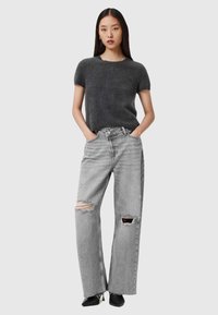 Grijze kortlopende gebreide top gecombineerd met hoge taille, distressed grijze denim jeans. De jeans hebben scheuren en rafelige zomen. Het model draagt zwarte schoenen.