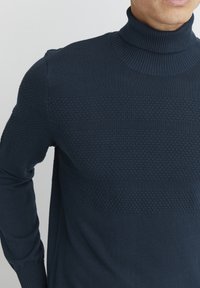 Maglione a collo alto blu navy realizzato in materiale lavorato a maglia, con motivi orizzontali testurizzati e polsini e colletto a costine.