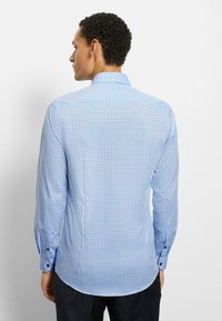 Hellblaues Hemd mit kleinem geometrischem Muster, langen Ärmeln und klassischem Kragen. Der Stoff hat eine glatte Textur und Manschetten mit Knöpfen.