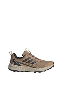 Terrex hiking shoe with a tan mesh upper, black accents, and a rubber sole. Features a padded collar and lace-up closure.