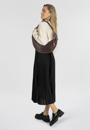 Brown leren schoudertas met ingebrand logo, gevlochten schouderriem en kleurrijke charme accenten. Geplooide zwarte rok en stevige zwarte schoenen.