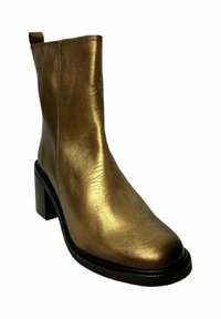 Botín de tobillo en dorado metálico con parte superior de cuero suave, punta cuadrada y tacón cuadrado. Presenta una trabilla trasera y suela negra.