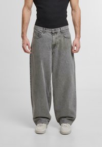 Jean en denim gris amples avec une taille haute, de grandes poches avant et des poignets élastiques, associés à des baskets blanches et un haut noir ajusté.