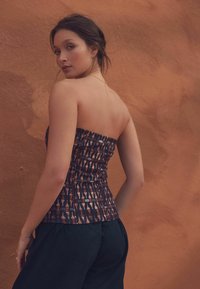 Strapless top van een gestreepte stof met geometrische ontwerpen in donkere en lichte tinten; aangesloten stijl. Zwarte broek aanvult de outfit.
