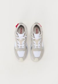 Helle graue Sneaker mit weißen Netz- und Wildlederakzenten, ausgestattet mit einer Gummisohle, weißen Schnürsenkeln und rotem Branding auf der Innenseite.