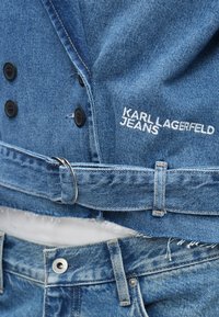 Džinsu jaka ar melnajām pogām, ar "KARL LAGERFELD JEANS" izšuvumu. Iekļauti jostas cilpas un novecojuša apakšmala.