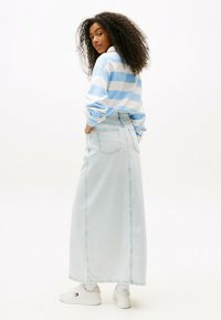 Chemise à rayures bleu clair et blanche à manches longues associée à une jupe maxi en denim clair taille haute et des baskets blanches. Cheveux bouclés texturés.