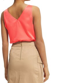 Haut sans manches fuchsia avec un col en V et une texture lisse, associé à une jupe beige dotée d'une fermeture éclair au dos et de poches latérales.