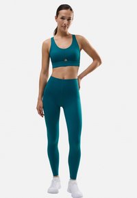 Conjunto de sujetador deportivo y leggings en color verde azulado, diseño ajustado, textura suave, con un detalle de corte en el sujetador y cintura elástica en los leggings.