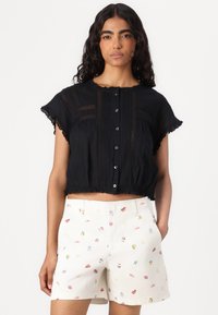 Top cropped nero con pizzo, caratterizzato da pannelli testurizzati e bottoni. Abbinato a pantaloni corti crema, decorati con motivi floreali colorati.