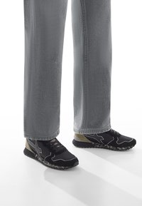 Černé sportovní boty s šedými detaily a sole v kamuflážovém vzoru, doplněné o světle šedé široké džíny.