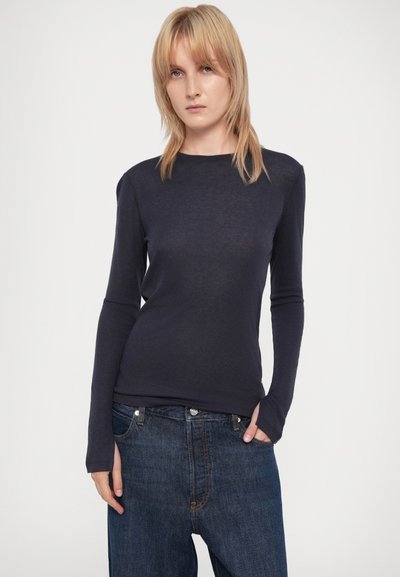 Cămașă navy cu mânecă lungă, cu un design ajustat și gât rotund, asociată cu blugi dark blue, cu o croială lejera. Textură netedă, detalii minime.