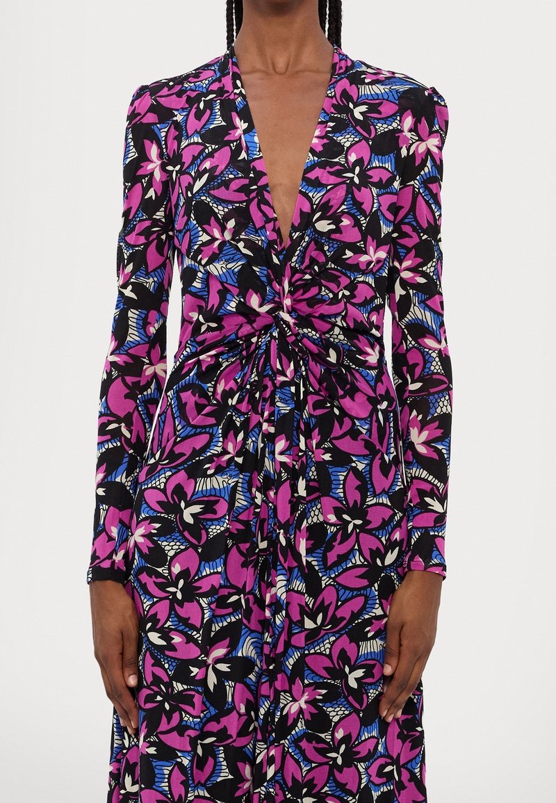 Blommig klänning med djup V-ringning, långa ärmar, svart bas och livliga rosa och blå blommönster med en knuten detalj vid midjan.
