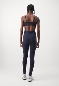 Black sports bra and high-waisted navy leggings. Smooth fabric with a fitted design. Model wearing white athletic shoes.
