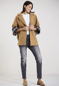 Tan, fuzzy wool blend jacket with wide plaid cuffs, white shirt, and gray jeans. Tan loafers complete the outfit. Simple, relaxed design.