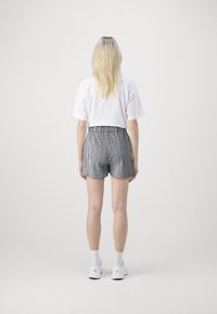 T-shirt blanche raccourcie associée à un short à carreaux noir et blanc. Le short présente une taille élastique et une texture subtile. Des baskets blanches complètent la tenue.