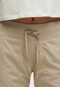 Beige kötőzsinóros nadrág bordázott derékpánttal, textúrált anyaggal és két oldalsó varrással, ezüst hegyekkel a kötőzsinórokon.