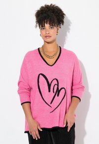 Rosa stickad tröja med V-hals och svarta detaljer. Har en stor svart hjärtdesign framtill och ribbade ärmslut.