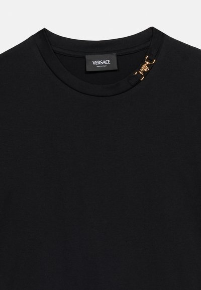T-shirt noir col rond avec étiquette Versace et détail de chaîne en or avec tête de Méduse près de l'encolure du côté droit.