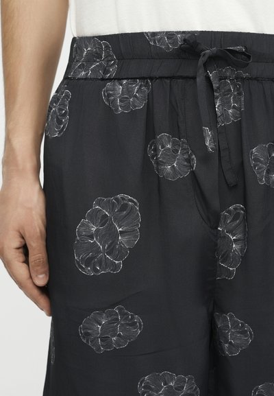 Κοντινό πλάνο μαύρου παντελονιού με λευκά λουλουδάτα σχέδια και ελαστική μέση δεμένη με φιόγκο στη δεξιά πλευρά.